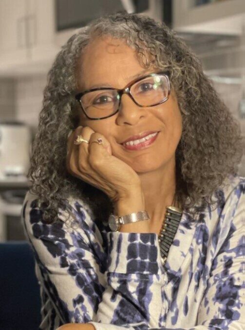 A woman with glasses sitting in front of a wall.